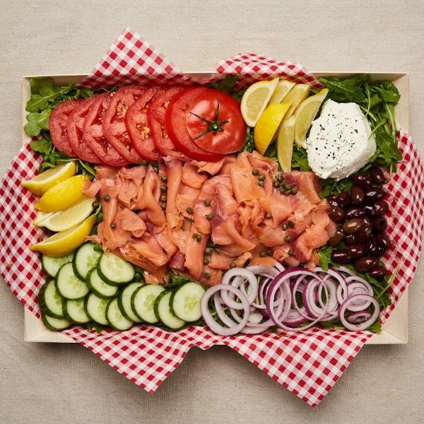 Plate of lox, capers, cream cheese, tomato, onion, cucumber, arugula, lemon wedges, and olives