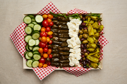 Mediterranean platter seen from above with grape leaves, feta cheese, olives, tomato, and pepperoncini