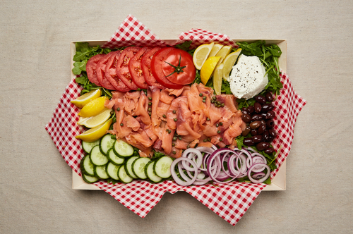 Plate of lox, capers, cream cheese, tomato, onion, cucumber, arugula, lemon wedges, and olives