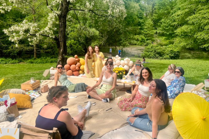 Group of women enjoying a picnic outdoors with balloons and cushions.