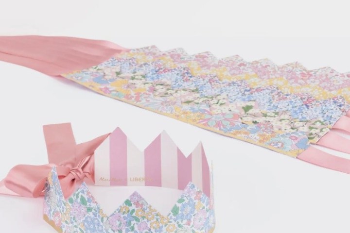 Floral paper crown with pink ribbon tied to gift wrap on white background.